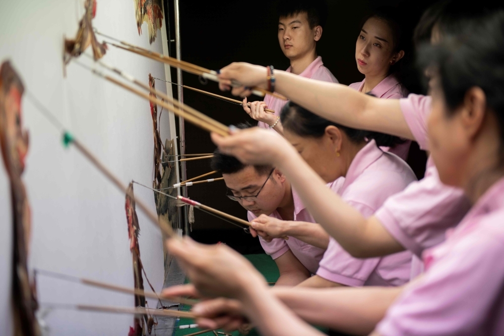 In this picture taken on May 9, 2019, Jin Xinchun, a member of the Flying Dragon Troupe, creates a shadow puppet at the troupe's studio on the outskirts of Beijing. Shadow puppets flitting across screens and reliving age old stories have fascinated Chinese people for some 2,000 years, but falling audiences mean troupes are having to be creative to stay on the stage. — AFP