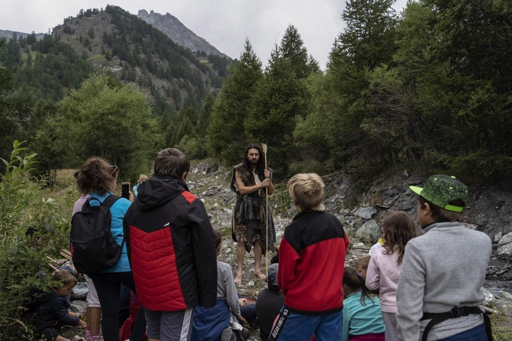 Guido Camia dressed as a Neanderthal Cave man gives a lesson to children in a wood in Chianale, in the Italian Alps, near the French border, on August 7. -AFP  