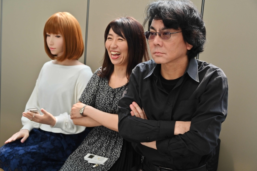 This photo taken on June 16, 2019 shows robotician Hiroshi Ishiguro (R) and his assistant (C) posing next to one of his robots at his research center in Osaka. Set in 2019, cult 80s movie 
