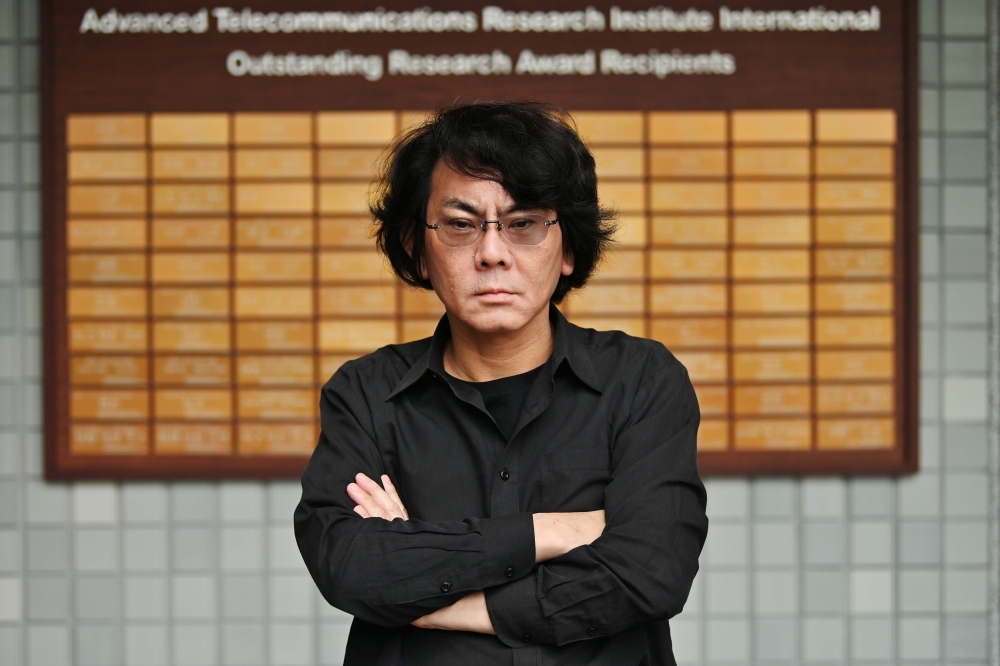 This photo taken on June 16, 2019 shows robotician Hiroshi Ishiguro (R) and his assistant (C) posing next to one of his robots at his research center in Osaka. Set in 2019, cult 80s movie 