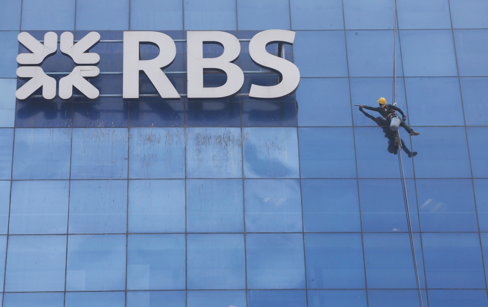 A worker cleans the glass exterior next to the logo of RBS (Royal Bank of Scotland) bank at a building in Gurugram on the outskirts of New Delhi, India, in this Sept. 8, 2017 file photo. — Reuters