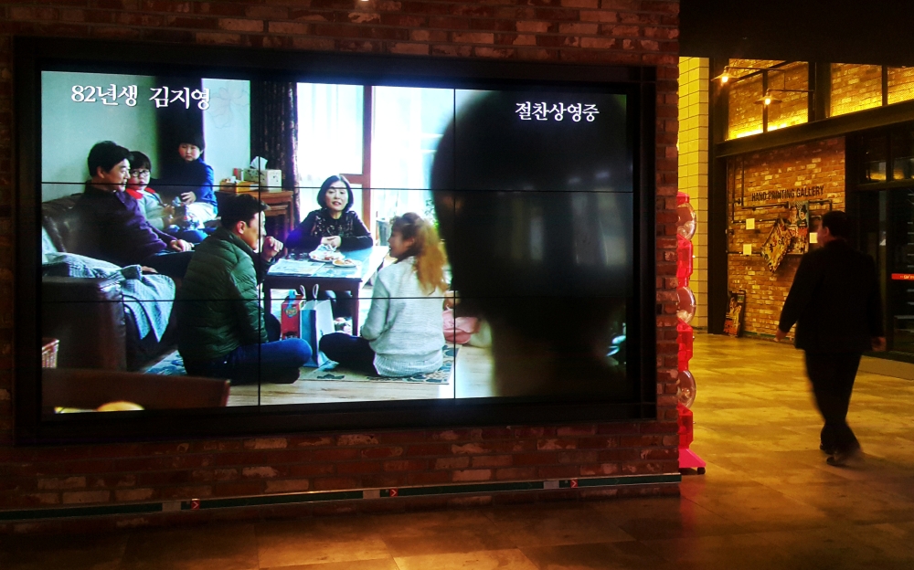 A moviegoer walks near a screen playing a trailer for 