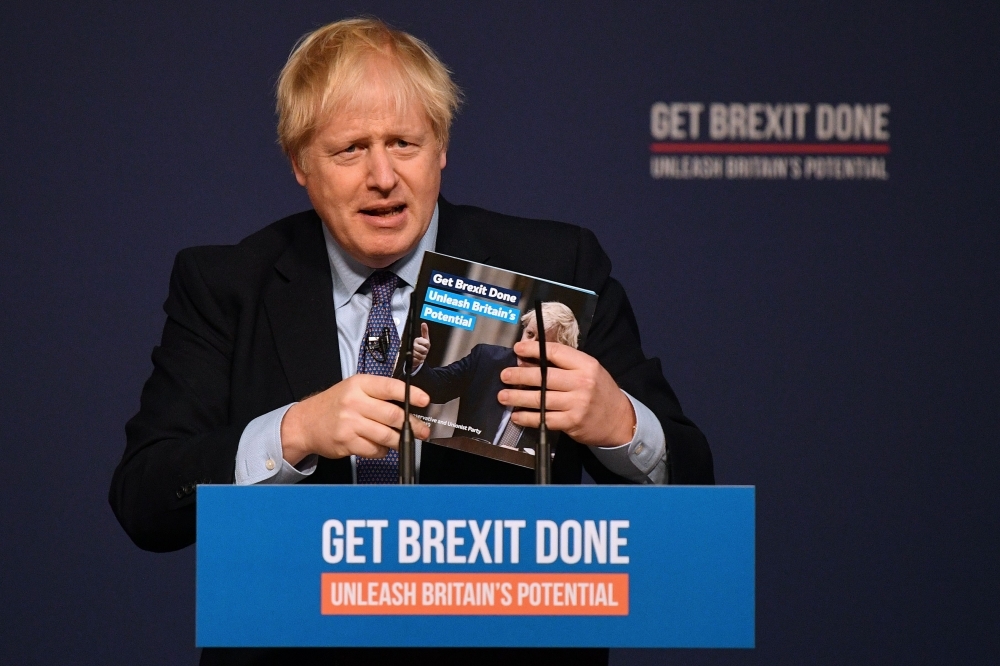 Britain's Prime Minister Boris Johnson holds a copy of the manifesto as he speaks during an event to launch the 2019 Conservative Party general election manifesto on Sunday. -AFP