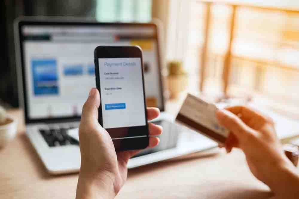 Man hands using smartphone and laptop computer for online shopping at home. Hand holding mobile phone with Payment Detail page display and credit card, online shopping concepts.