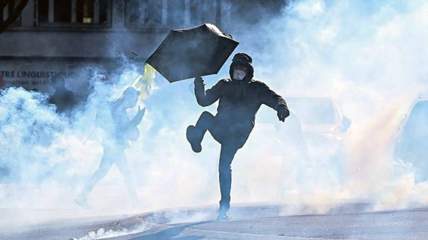 A protester with an umbrella kicks away a teargas pellet during a demonstration on the third day of nationwide rallies. — courtesy AFP