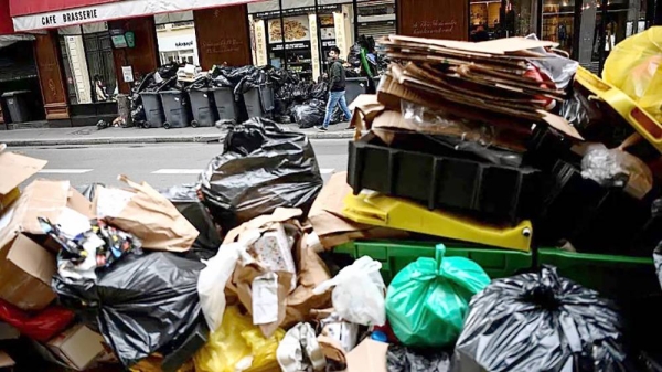 A man (top) walks past a pile of garbage bags that have been piling up since waste collectors went on strike. — AFP