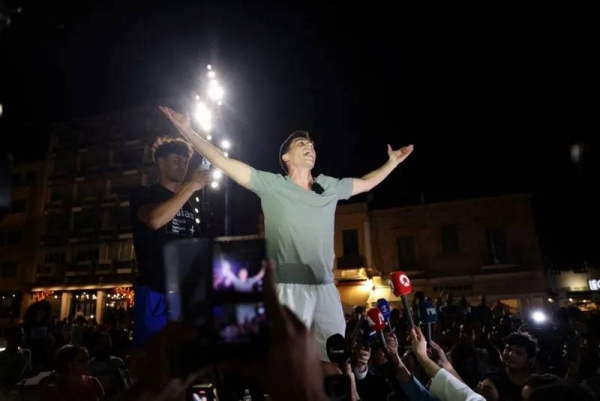 Fidias Panayuotou standing in front of some microphones with his arms raised in the air at a rally