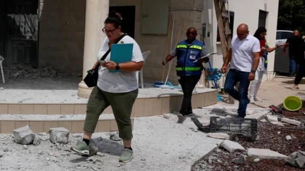 People walk near a damaged building in northern Israel after Hezbollah launched hundreds of rockets and drones toward Israel