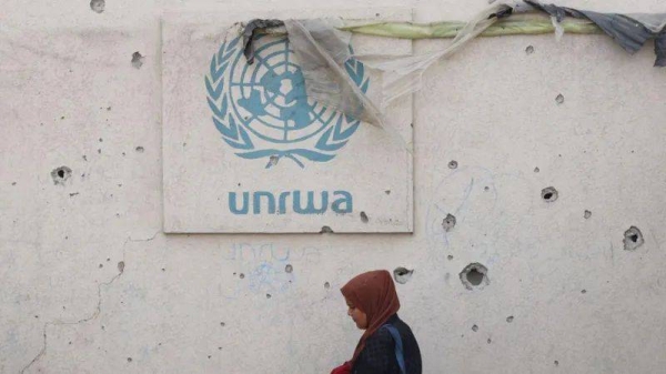 A Palestinian woman walks past a damaged wall bearing the Unrwa logo at a camp for internally displaced people in Rafah, southern Gaza Strip