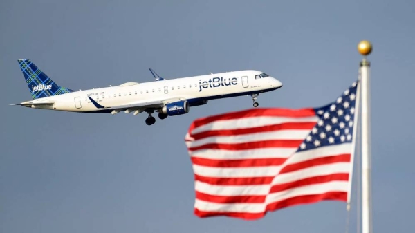 A JetBlue passenger jet flies past the US flag