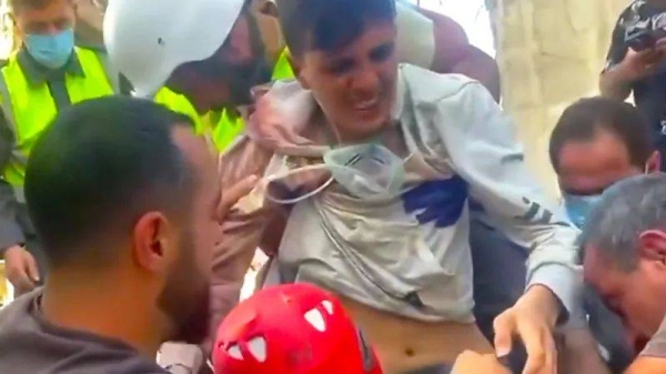 A young man is rescued from the rubble of an apartment block in El Karak