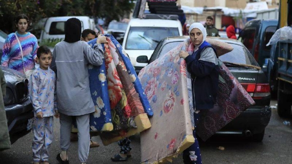 Displaced families carry mattresses as they prepare to return to their villages after a ceasefire between Israel and Hezbollah went into effect in Sidon, 27 November 2024