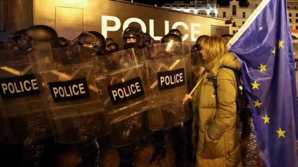 A protester in Tbilisi, Georgia stands in front of a line of riot police holding a large European Union flag