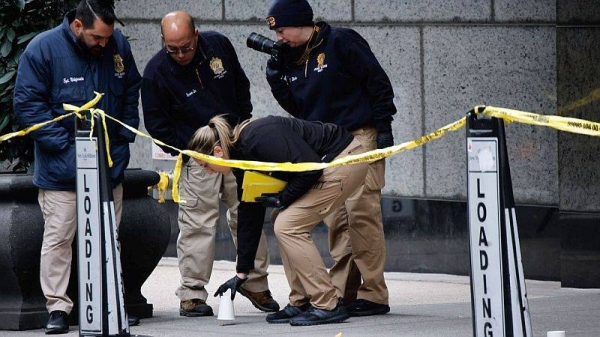 Members of the New York police crime scene unit pick up cups marking the spots where bullets lie as they investigate the scene outside the Hilton Hotel in midtown Manhattan where Brian Thompson was fatally shot