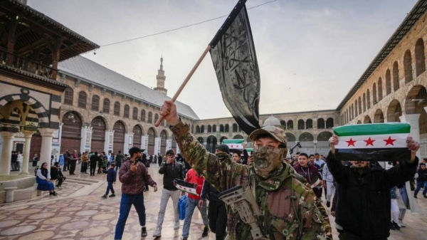 A masked opposition fighter carries a flag of Hayat Tahrir al-Sham (HTS) in the courtyard of the Umayyad Mosque in the old walled city of Damascus, Syria, 2024