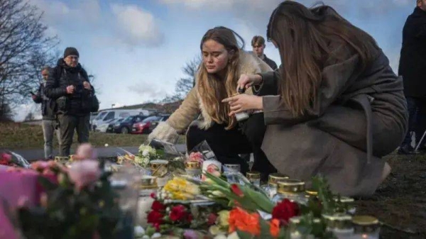 Two women place flowers beside a memorial for the victims of a mass shooting in Sweden