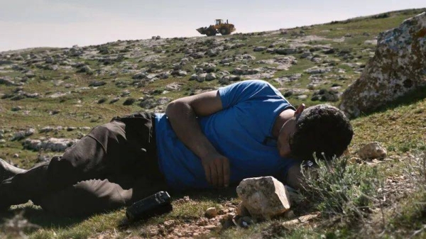 Basel Adra with his camera in his West Bank home, an Israeli army bulldozer behind him