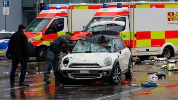 Two emergency service workers inspect a damaged white Mini Cooper