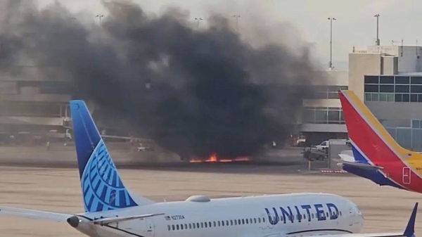 A frame from a video shows flames under a plane and black smoke rising at the Denver airport