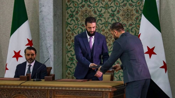 Syria's interim president Ahmad Al-Sharaa, center, prepares to sign a temporary constitution for the country in Damascus