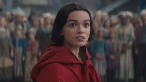 Disney Actor Rachel Zegler in Disney's live action Snow White film. She is wearing a red cape and silver necklace