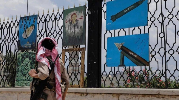 A Yemeni gunman walks past paintings depicting rockets and scenes in solidarity with Gaza, displayed on a roadside fence in Sanaa, Yemen, Monday, May 5, 2025