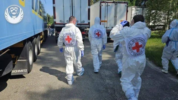 Red Cross members in protective suits walk towards refrigerator lorries with the bodies of killed Ukrainian soldiers