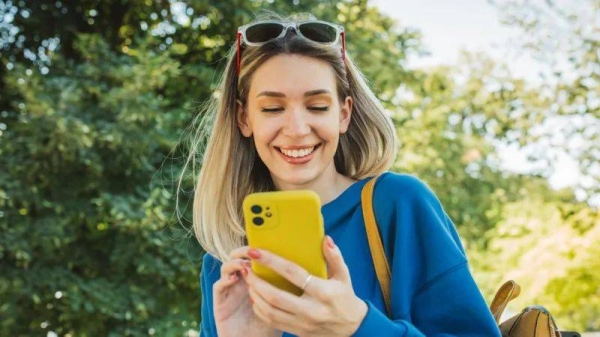 File photo of a young woman sitting on bench in park and using a yellow smartphone