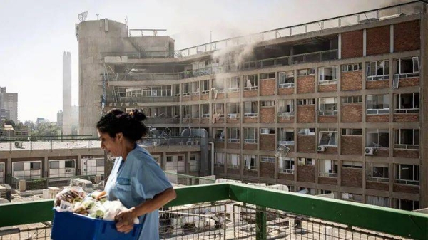 A nurse is carrying medical supplies past a building with smoke billowing out at Soroka Hospital following an Iranian missile attack in Beersheba, southern Israel, on 19 June, 2025
