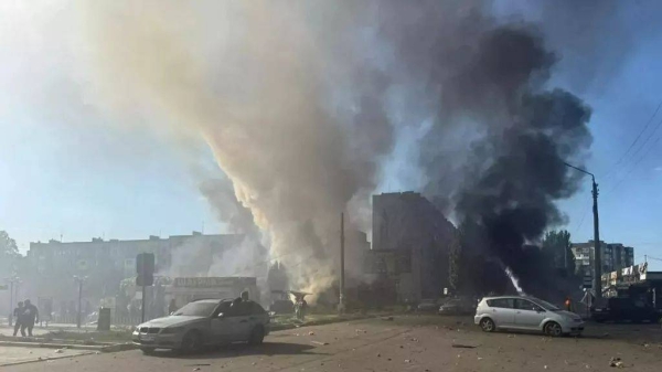 Two towering plumes of smoke billow from smoldering vehicles and storefronts in central Dobropillia after a 500-kg Russian airstrike on 16 July 2025