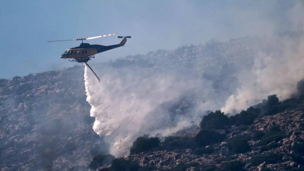 A firefighting helicopter drops water while battling a blaze in the seaside area of Charakas, 26 June, 2025