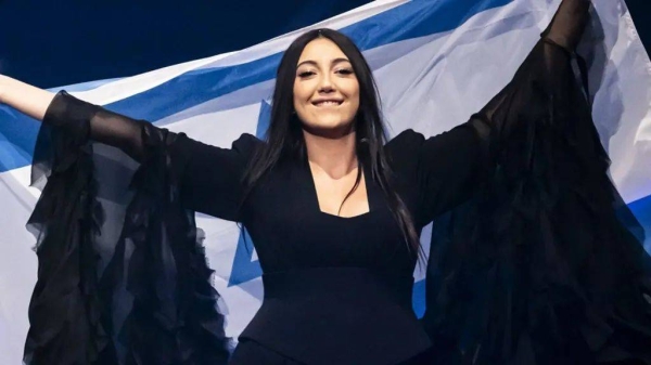 A woman with long dark hair smiling and holding up an Israeli flag behind her