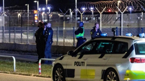 Police stand next to a fence outside an airport at night, a police vehicle is in the foreground